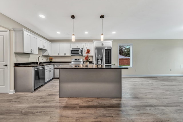 kitchen with light hardwood / wood-style floors, white cabinetry, hanging light fixtures, and appliances with stainless steel finishes