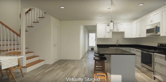 kitchen with white cabinetry, a center island, a breakfast bar, appliances with stainless steel finishes, and light wood-type flooring