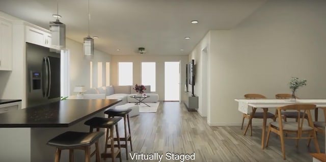 kitchen featuring pendant lighting, white cabinets, light hardwood / wood-style floors, stainless steel fridge with ice dispenser, and a breakfast bar area