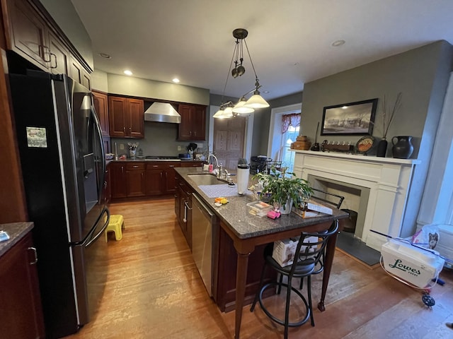 kitchen with sink, wall chimney range hood, a kitchen breakfast bar, refrigerator with ice dispenser, and an island with sink