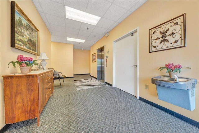 hallway with a paneled ceiling and dark colored carpet