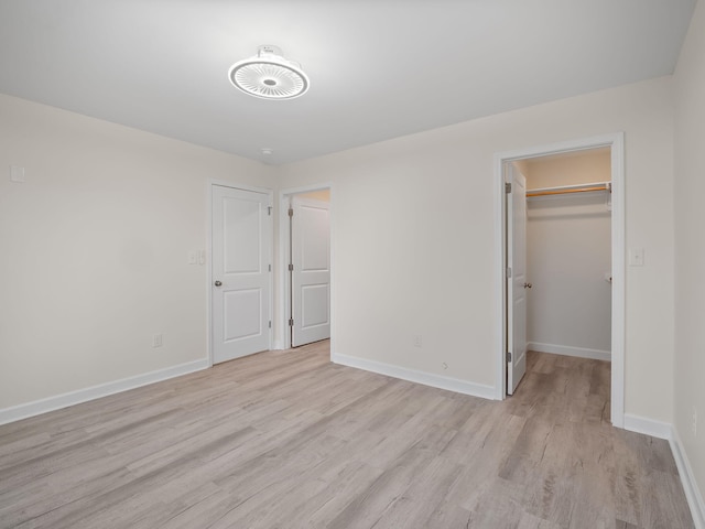 unfurnished bedroom featuring a closet, light wood-type flooring, and a walk in closet