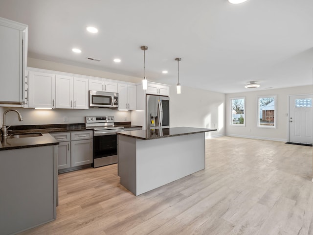 kitchen featuring sink, stainless steel appliances, pendant lighting, a kitchen island, and light wood-type flooring