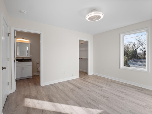 unfurnished bedroom featuring ensuite bathroom, sink, light wood-type flooring, a spacious closet, and a closet