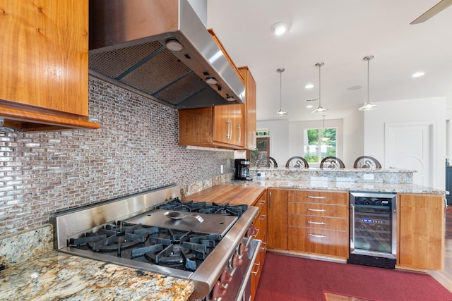 kitchen with stainless steel gas stove, wine cooler, kitchen peninsula, ventilation hood, and pendant lighting