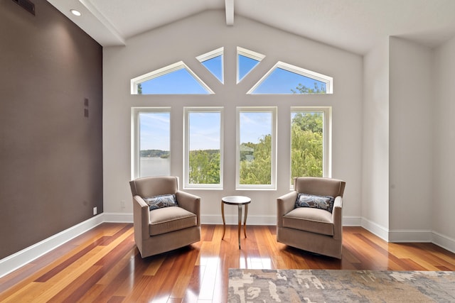 sitting room featuring a water view, vaulted ceiling with beams, wood-type flooring, and plenty of natural light