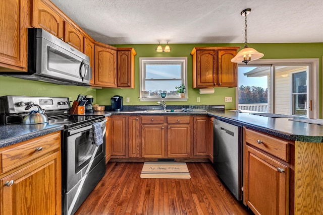 kitchen with appliances with stainless steel finishes, a textured ceiling, plenty of natural light, and dark hardwood / wood-style floors