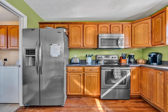 kitchen featuring washer / dryer, appliances with stainless steel finishes, a textured ceiling, and hardwood / wood-style flooring