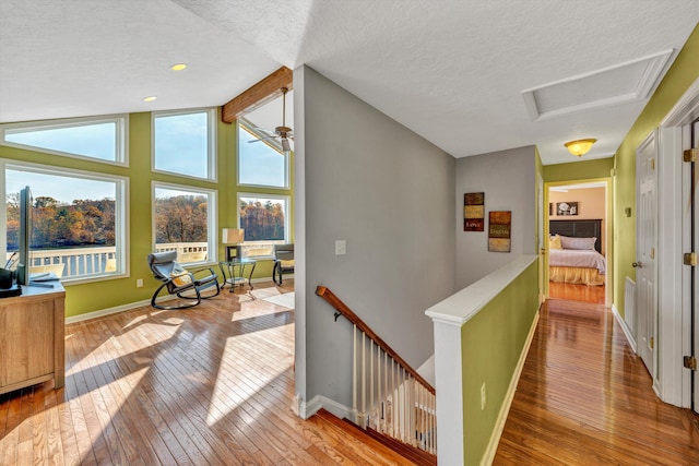 hall with vaulted ceiling, light hardwood / wood-style floors, and a textured ceiling