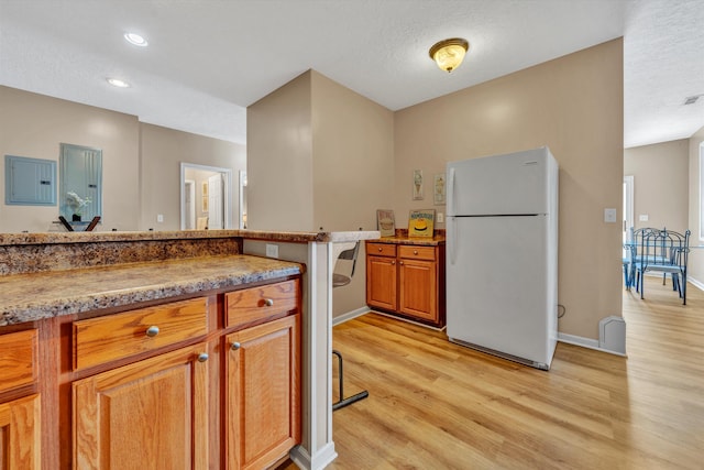 kitchen featuring light wood-type flooring, white refrigerator, and stone counters