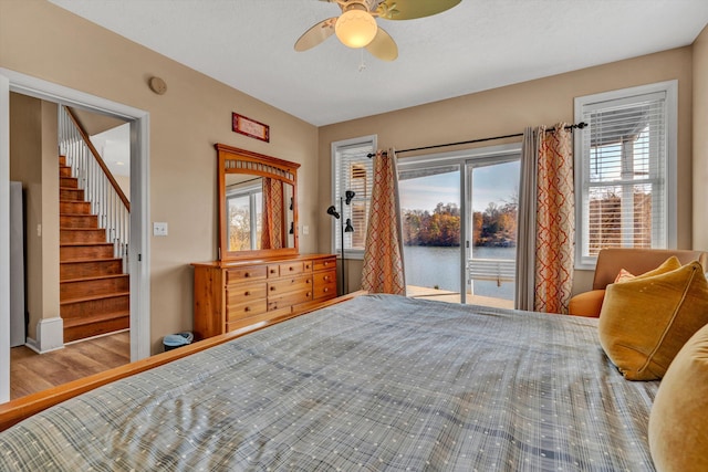 bedroom with access to outside, ceiling fan, light wood-type flooring, and a water view