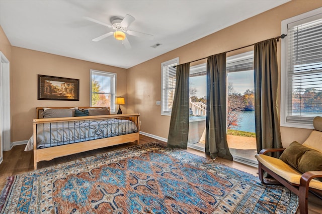 bedroom featuring dark hardwood / wood-style floors, a water view, access to exterior, and ceiling fan