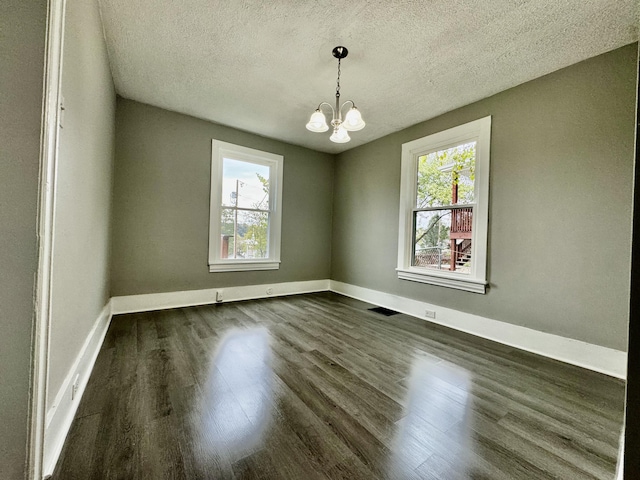 unfurnished room featuring a textured ceiling, dark hardwood / wood-style floors, and a chandelier