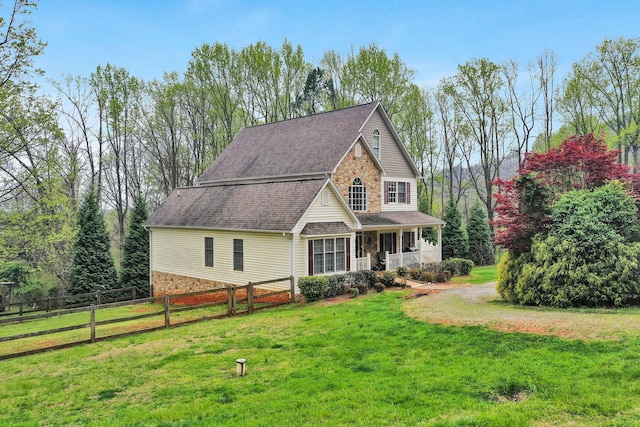 view of front of home featuring stone siding, fence, a front lawn, and covered porch