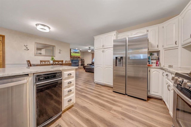 kitchen with white cabinets, a stone fireplace, light wood-type flooring, and stainless steel appliances