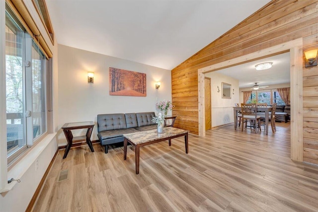 living room with wood walls, plenty of natural light, light hardwood / wood-style floors, and vaulted ceiling