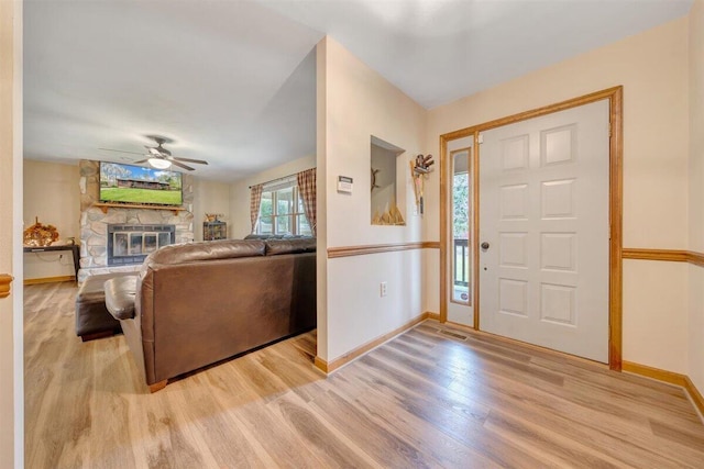 foyer featuring ceiling fan, light hardwood / wood-style floors, and a stone fireplace