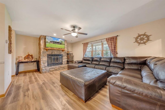 living room with light wood-type flooring, a stone fireplace, and ceiling fan