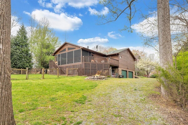 rear view of property featuring a sunroom, a fire pit, a yard, a wooden deck, and a garage