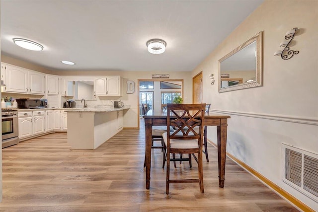 kitchen with light stone countertops, white cabinetry, stainless steel appliances, light hardwood / wood-style floors, and a breakfast bar area