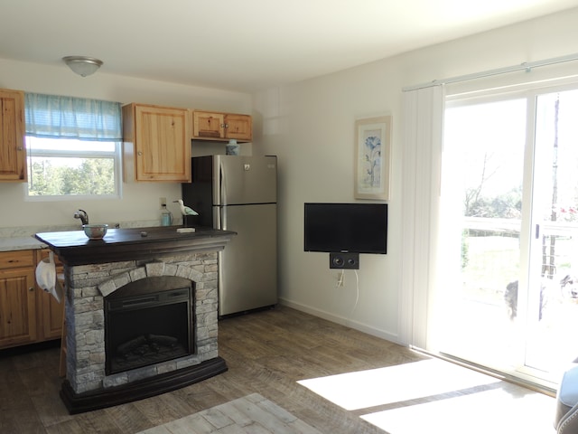 kitchen featuring stainless steel fridge, dark hardwood / wood-style flooring, and a stone fireplace