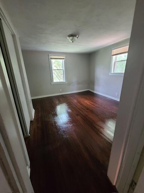 empty room with a healthy amount of sunlight, dark wood finished floors, and baseboards