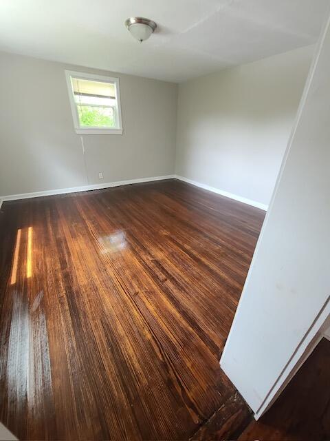 empty room with dark wood-type flooring and baseboards