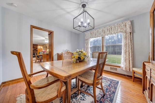 dining space with ceiling fan with notable chandelier and light hardwood / wood-style flooring