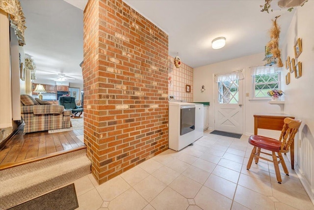 interior space with ceiling fan, light tile patterned flooring, a brick fireplace, brick wall, and separate washer and dryer