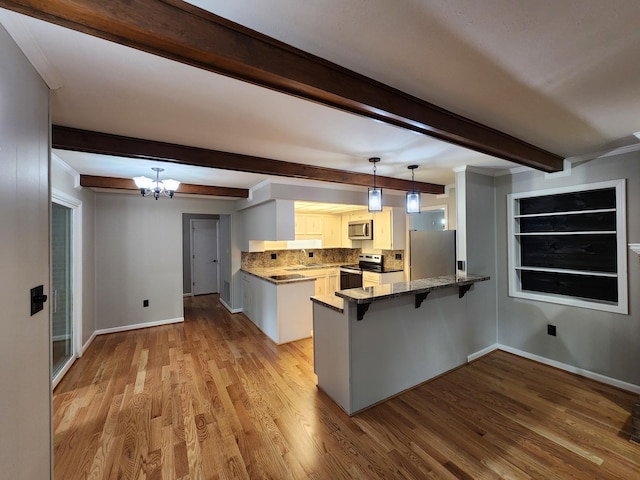 kitchen with kitchen peninsula, appliances with stainless steel finishes, a breakfast bar, pendant lighting, and a notable chandelier