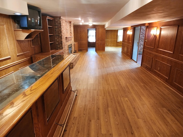 bar featuring wood walls, light wood-type flooring, and a brick fireplace