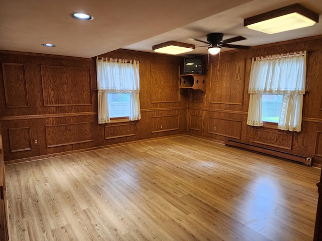 interior space featuring baseboard heating, wooden walls, ceiling fan, and light wood-type flooring