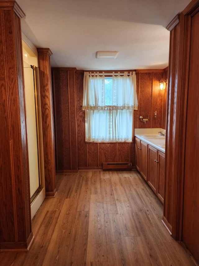 kitchen with baseboard heating, wooden walls, sink, and light wood-type flooring