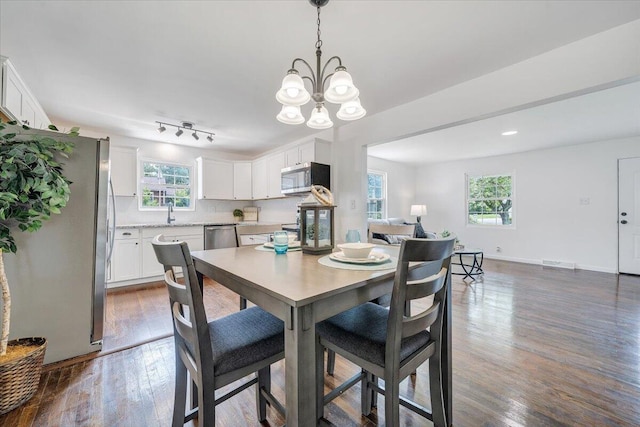 dining space with an inviting chandelier, dark hardwood / wood-style floors, and rail lighting