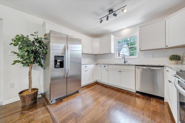 kitchen with white cabinetry, stainless steel appliances, hardwood / wood-style flooring, light stone counters, and rail lighting