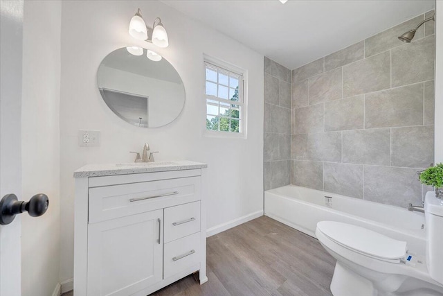 full bathroom featuring tiled shower / bath, vanity with extensive cabinet space, hardwood / wood-style flooring, and toilet