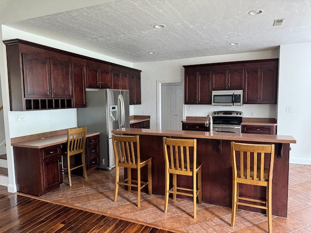 kitchen with a center island with sink, hardwood / wood-style floors, dark brown cabinetry, and stainless steel appliances