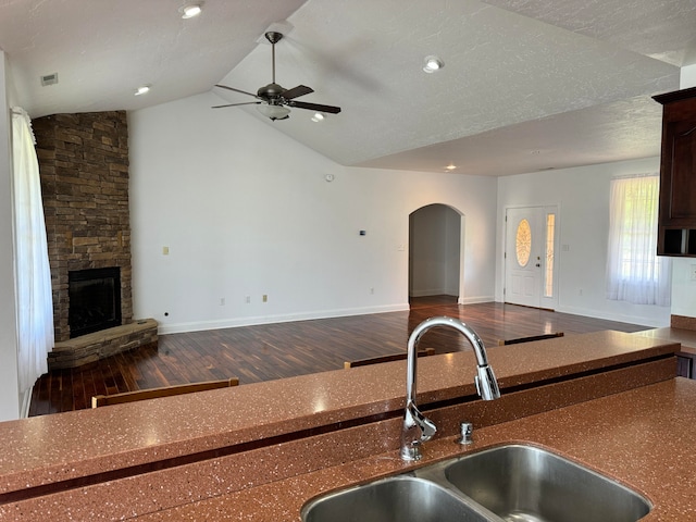 kitchen with dark wood-type flooring, a stone fireplace, ceiling fan, and lofted ceiling