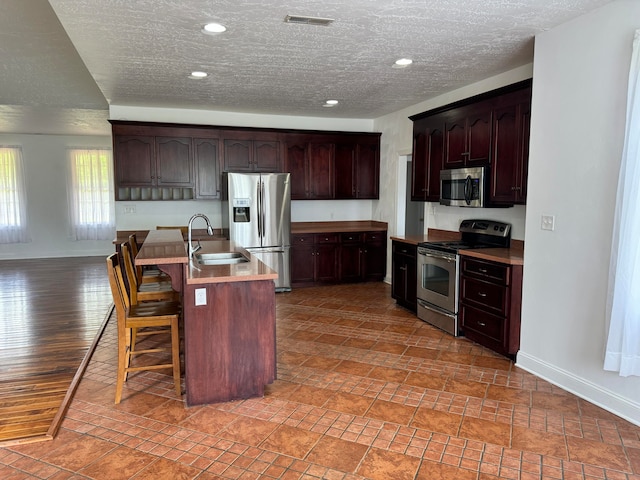 kitchen featuring a kitchen breakfast bar, dark brown cabinets, stainless steel appliances, sink, and a kitchen island with sink