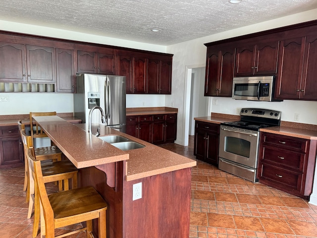 kitchen with stainless steel appliances, light tile flooring, a kitchen bar, sink, and a kitchen island with sink