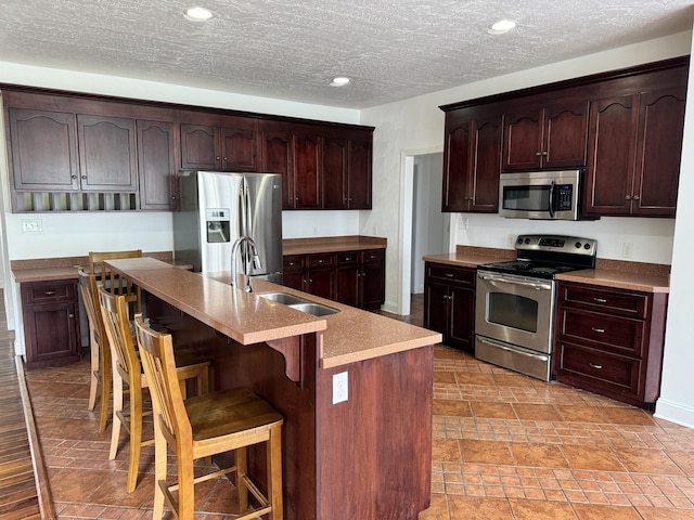 kitchen with stainless steel appliances, an island with sink, a breakfast bar area, sink, and light tile floors