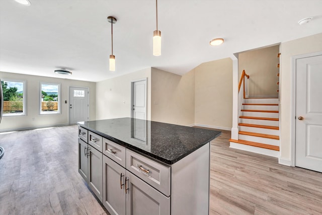 kitchen with pendant lighting, gray cabinets, dark stone countertops, light hardwood / wood-style floors, and a kitchen island