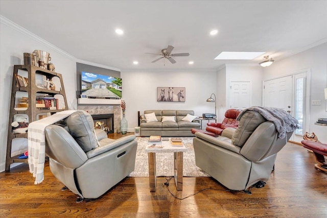 living room featuring dark hardwood / wood-style flooring, a skylight, ceiling fan, crown molding, and a high end fireplace