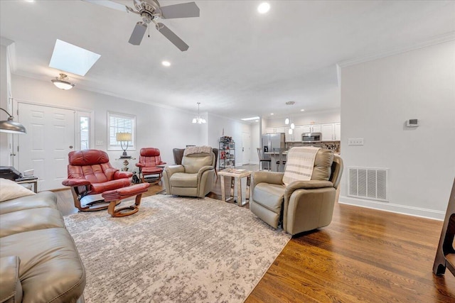 living room featuring dark hardwood / wood-style floors, ceiling fan, crown molding, and a skylight