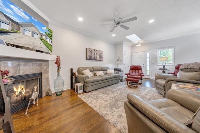 living room with crown molding, ceiling fan, a tiled fireplace, and hardwood / wood-style floors