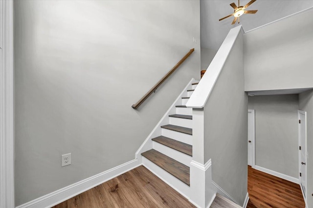 staircase with wood finished floors, a ceiling fan, and baseboards