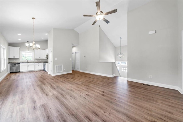 unfurnished living room with high vaulted ceiling, ceiling fan with notable chandelier, visible vents, baseboards, and light wood-style floors