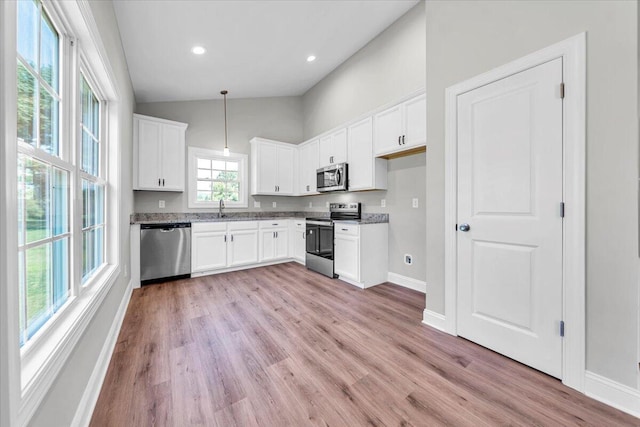 kitchen featuring light wood finished floors, stainless steel appliances, hanging light fixtures, white cabinets, and a sink