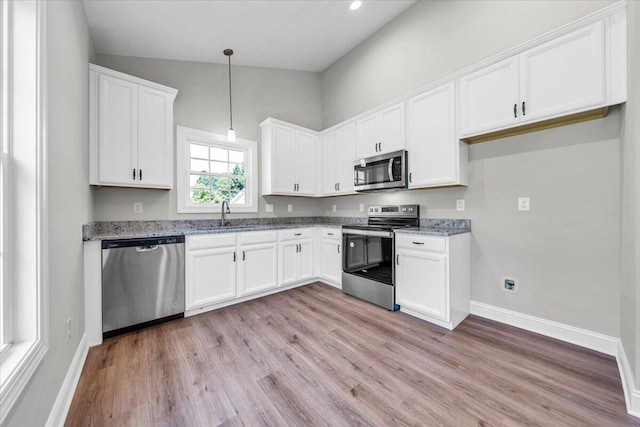 kitchen with stainless steel appliances, a sink, white cabinetry, dark stone counters, and pendant lighting