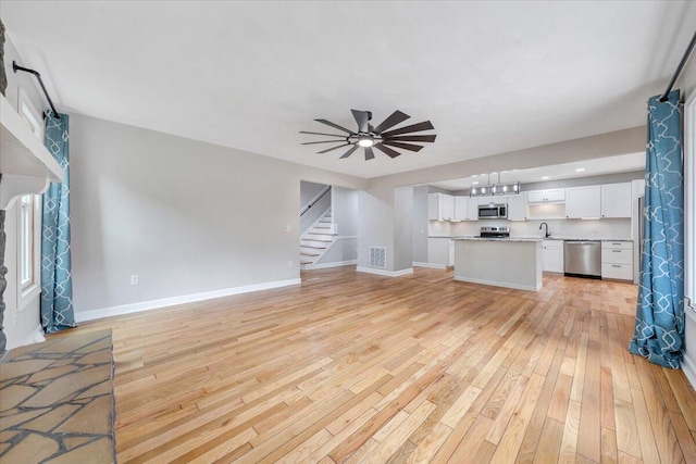 unfurnished living room featuring a sink, a ceiling fan, baseboards, stairway, and light wood finished floors